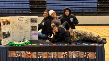 PISA Members standing with their backs against one another while tabling, one member is laying across the table. 