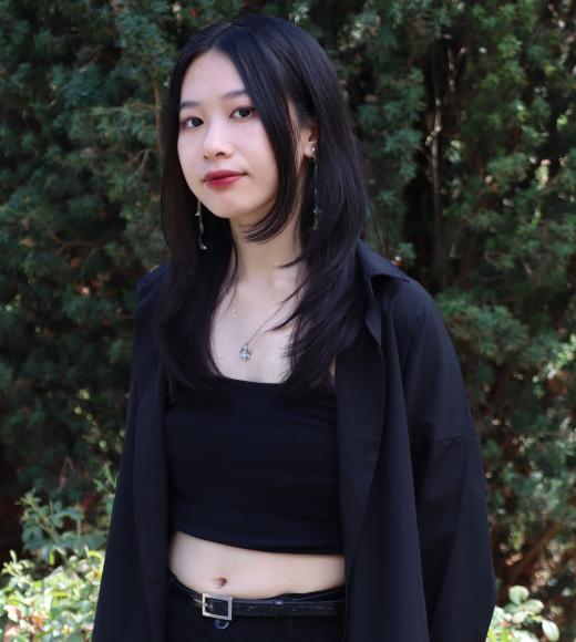 Profile picture of luna standing in front of a giant tall green tree and she is wearing a black shirt, pants, and cardigan