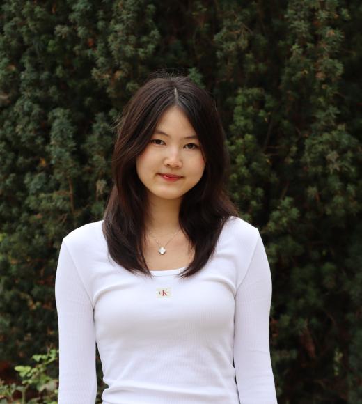 profile picture of Sophie standing in front of a tall green tree, she is wearing a white long sleeve blouse